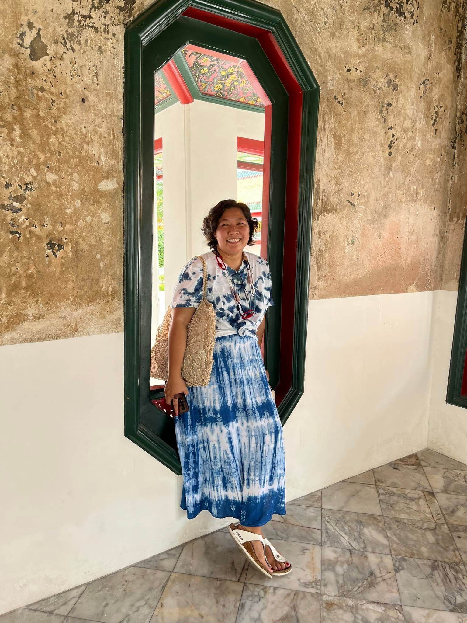 Woman in a tie-dye dress poses by a window.
