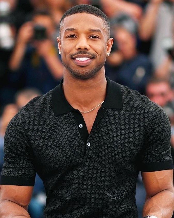 A portrait of Michael B Jordan wearing black polo shirt.