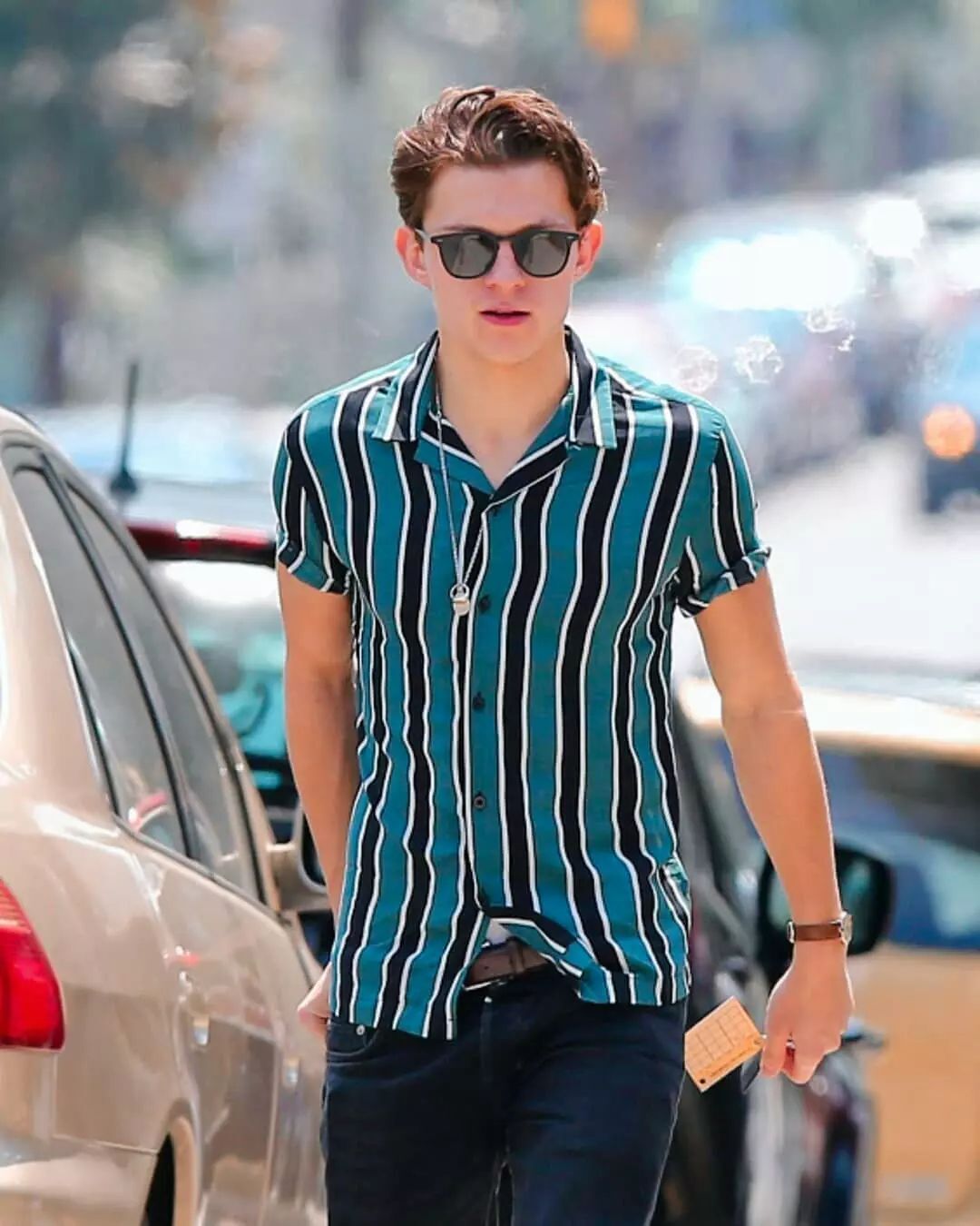 A portrait of Tom Holland wearing striped shirt and jeans.