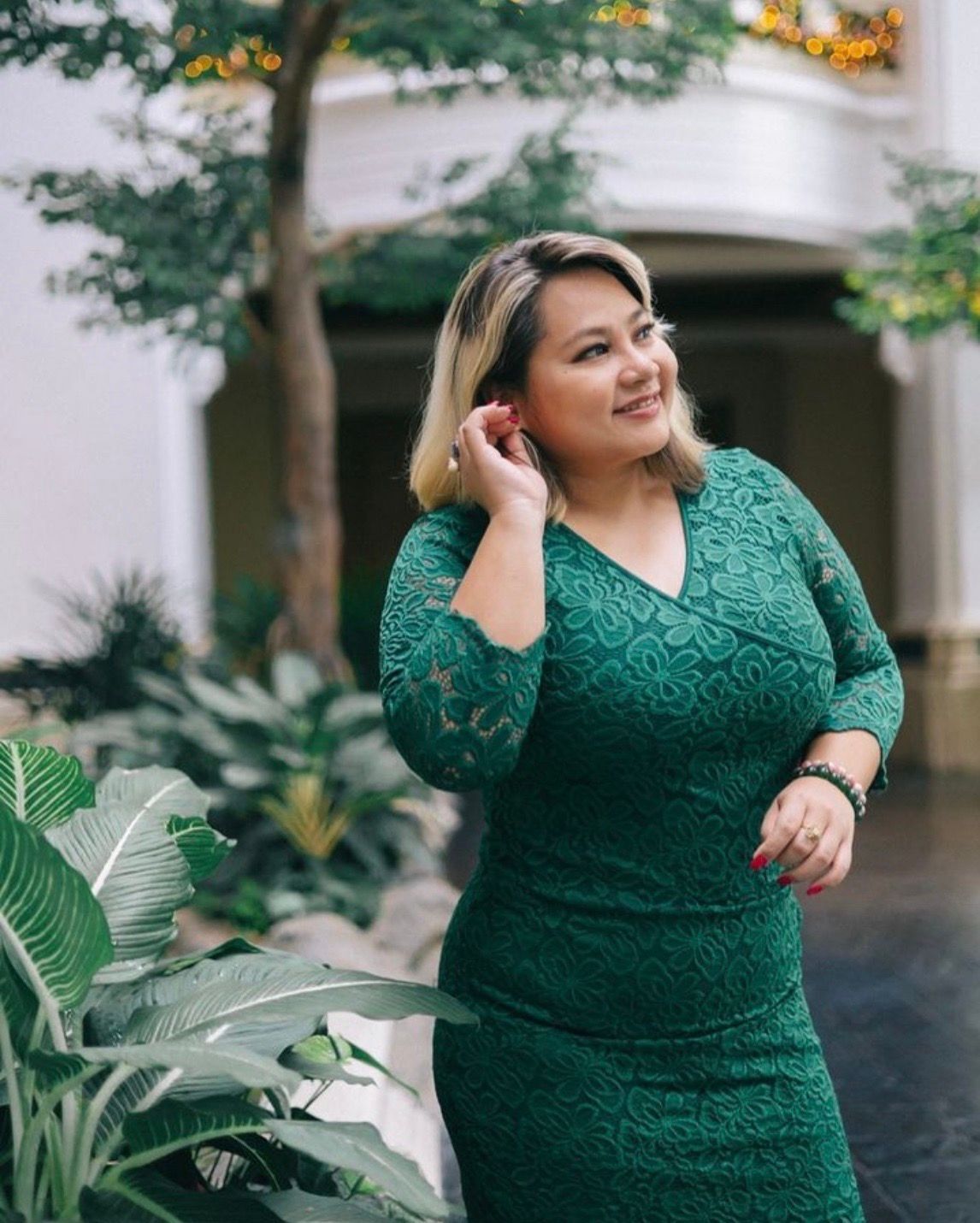 Portrait of a happy Asian woman smiling and looking away next to greenery.
