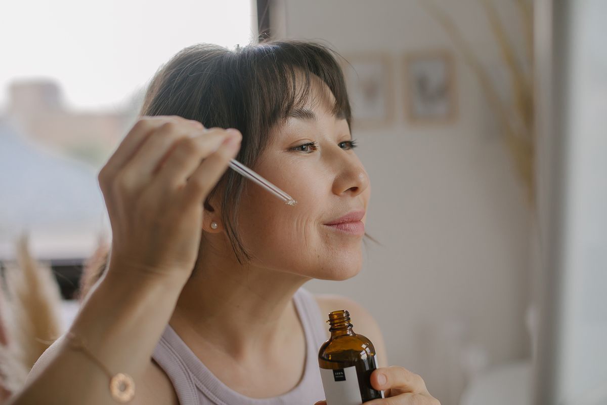 Asian woman applies serum on face