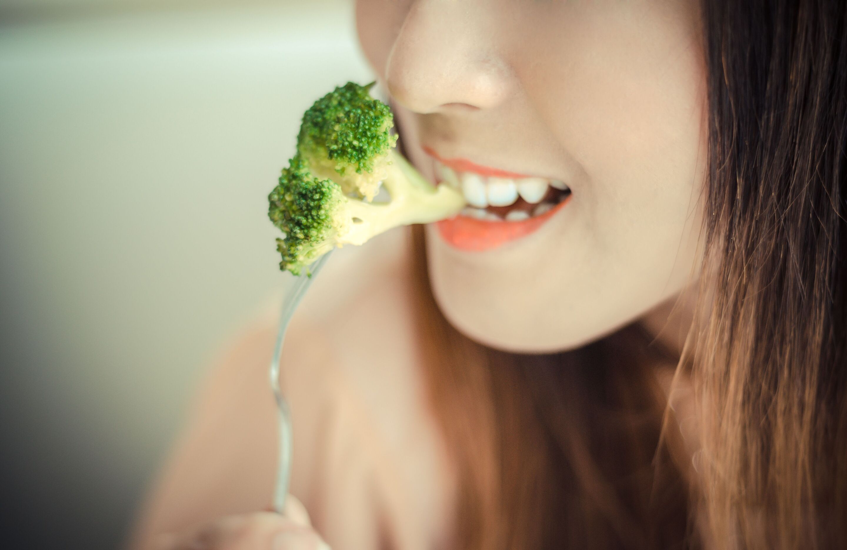 Close up shot of an Asian woman eating broccoli with a fork