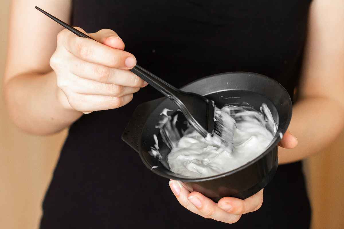 Woman mixing hair dye inside a black plastic bowl with a dye brush.