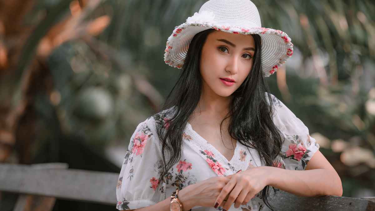 Woman wearing floral dress and white hat posing in front of the camera.