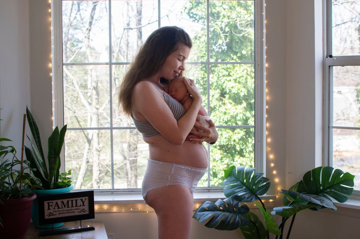 Mom carrying newborn in diaper and nursing bra.