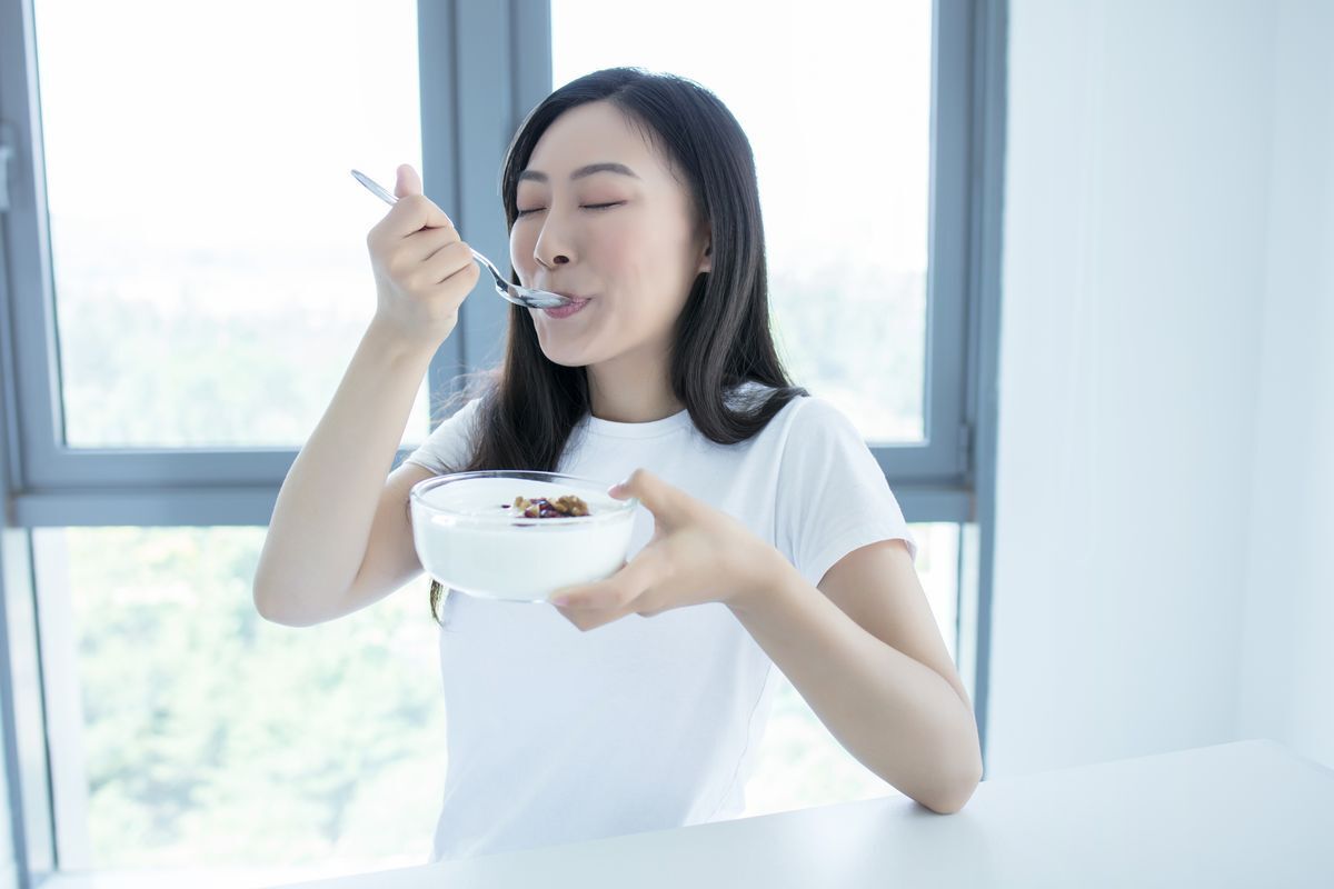 Asian woman eating from a bowl of yogurt.