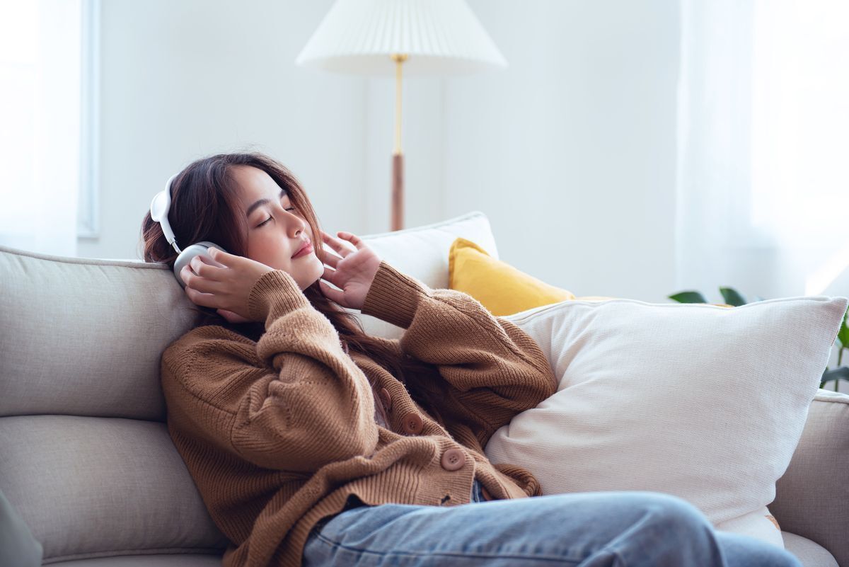 Filipino woman relaxed on sofa listening to headphones.