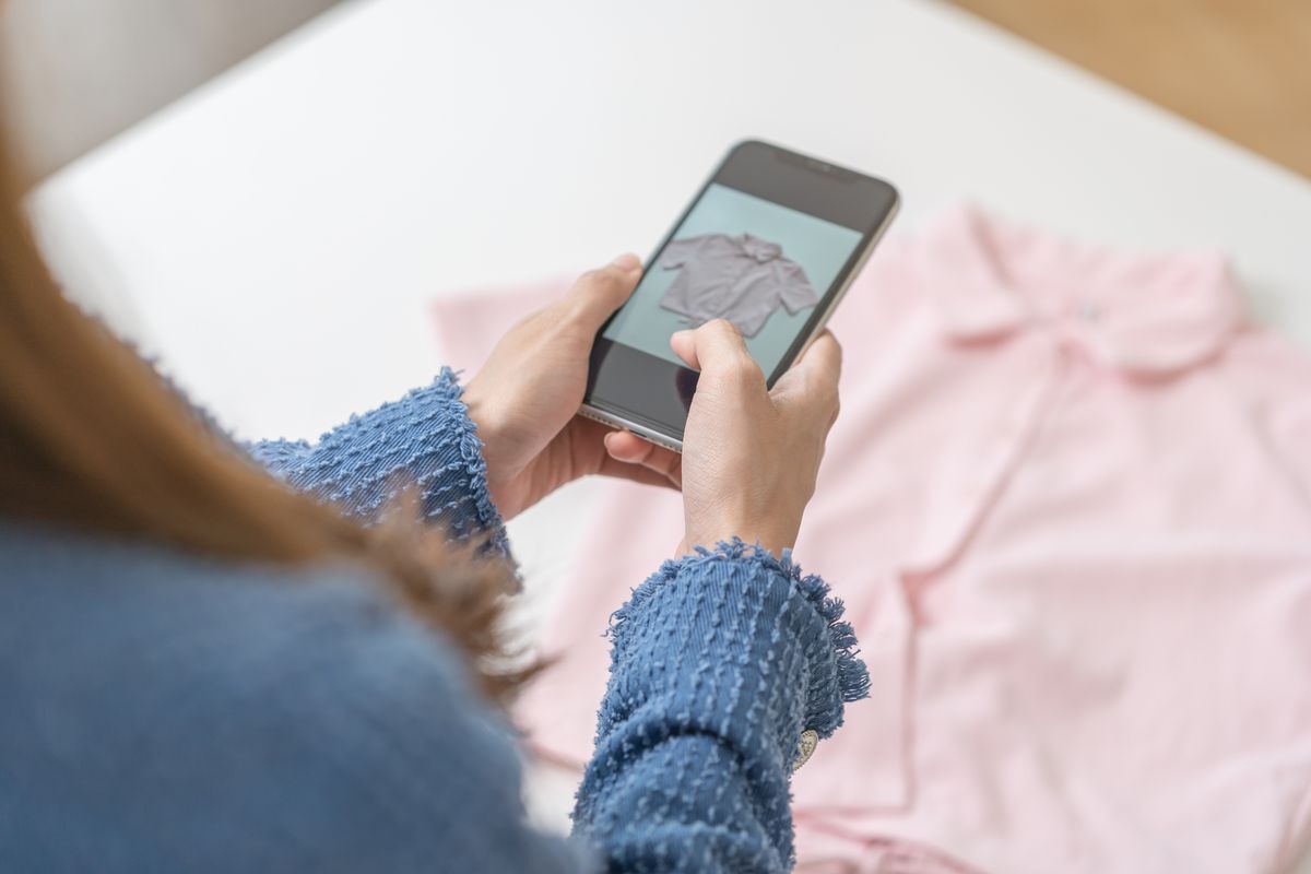 Closeup of a woman’s hands taking a photo of a pink shirt with her phone.