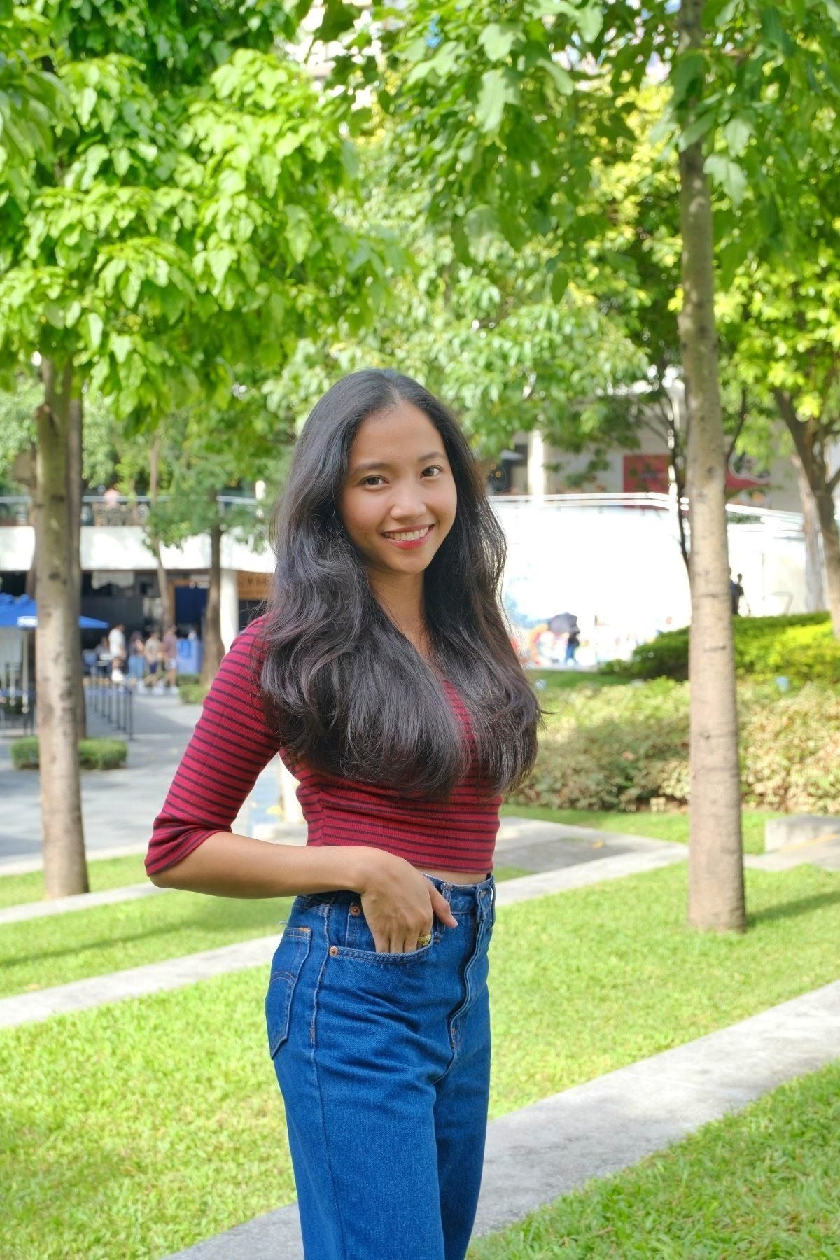 Smiling woman with long, black hair wearing a red top and a pair of jeans. 