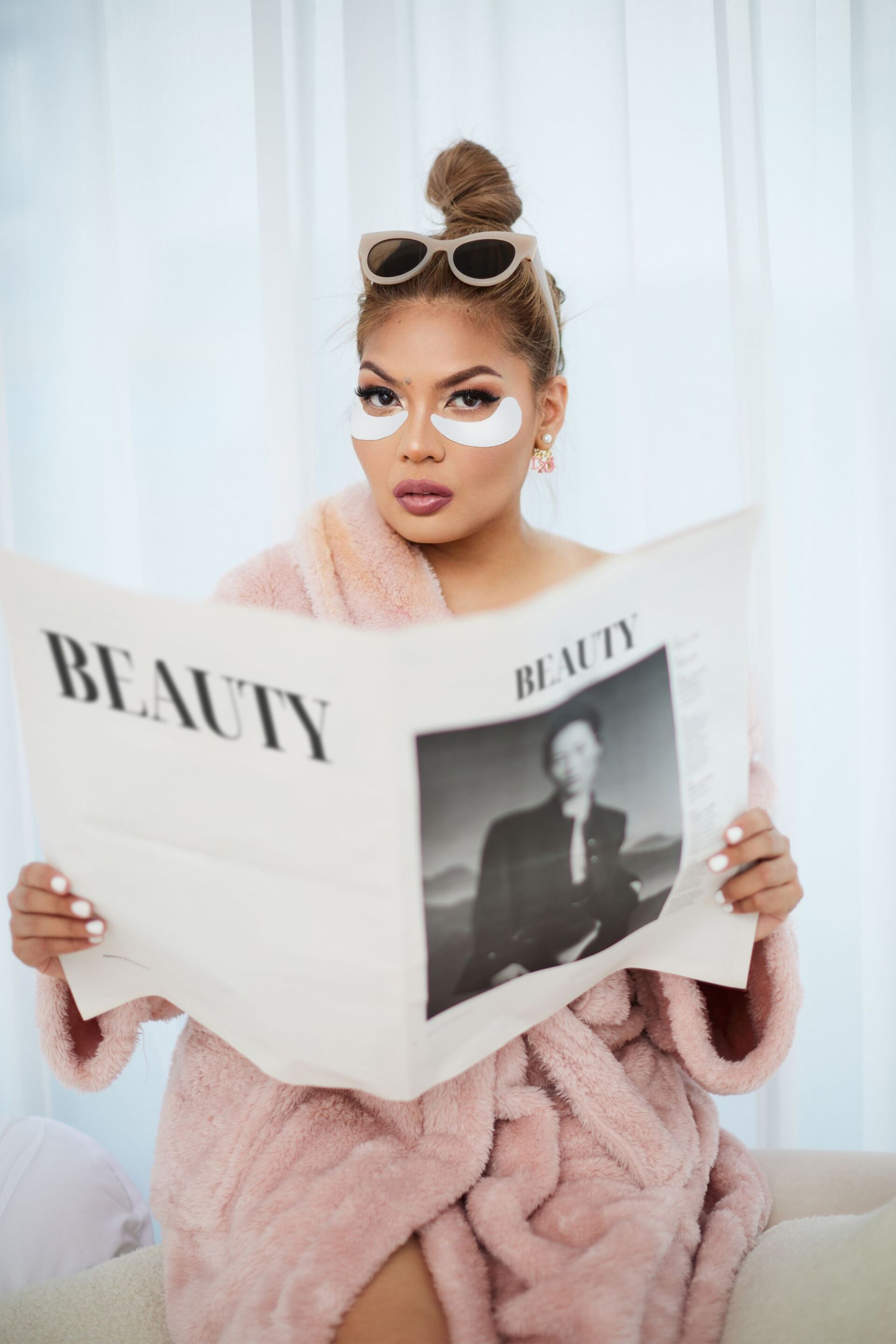 A portrait of woman in bathrobe and eye masks reading a newspaper.