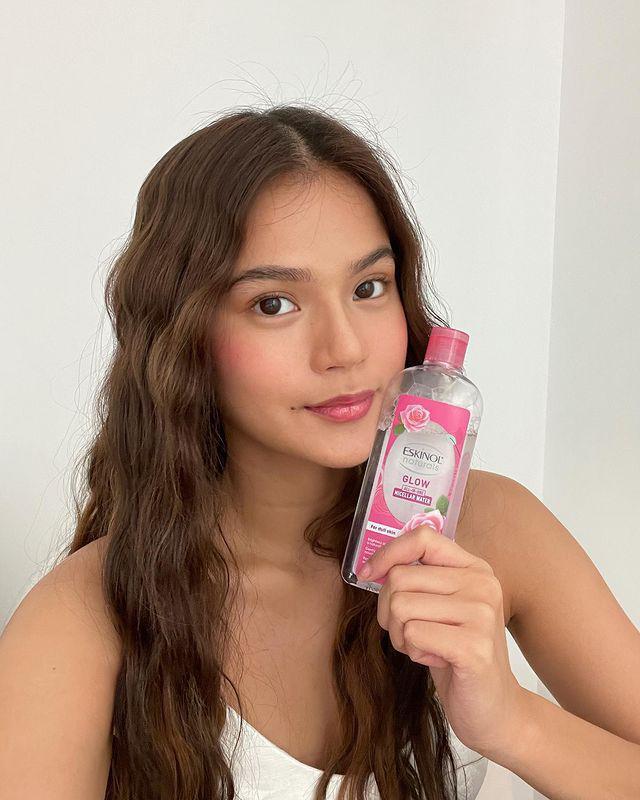 A woman with curly hair holding an Eskinol product