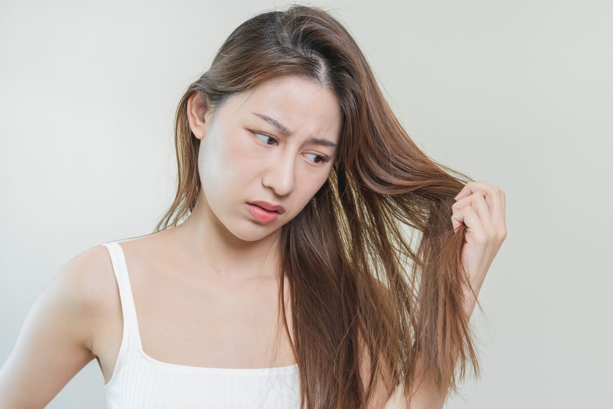 Asian woman looks worried, holds and touches her hair strands.