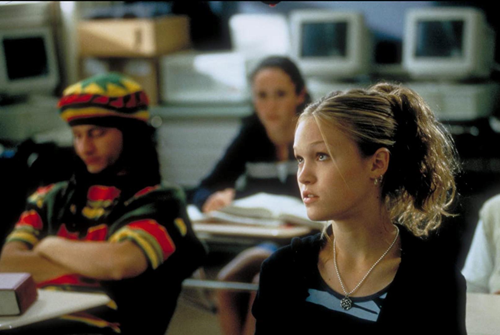 Julia Stiles with curly hair sitting in a classroom 