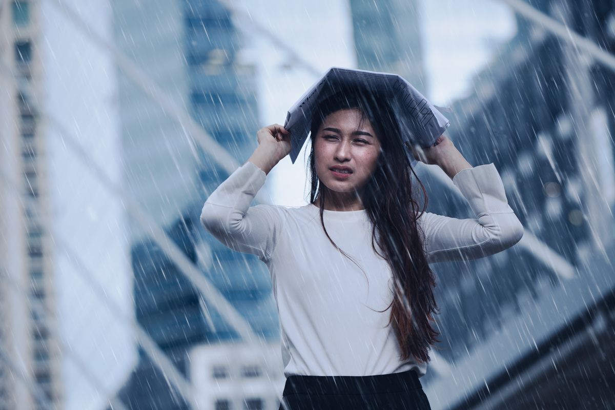 Filipino woman caught in the rain, covering her head with a newspaper.