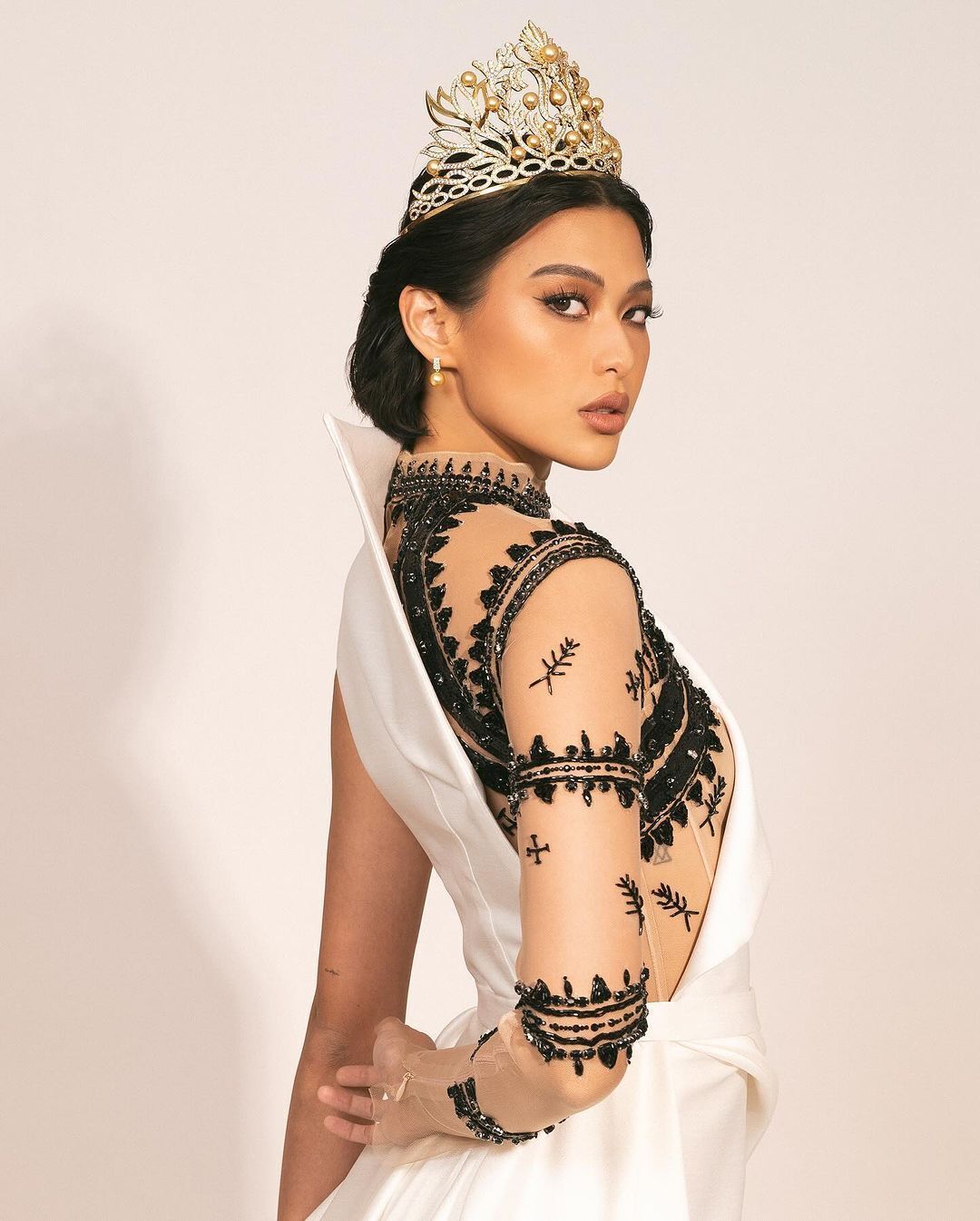 A portrait of Miss Universe Philippines 2023 Michelle Dee with lacey black dress and golden crown.
