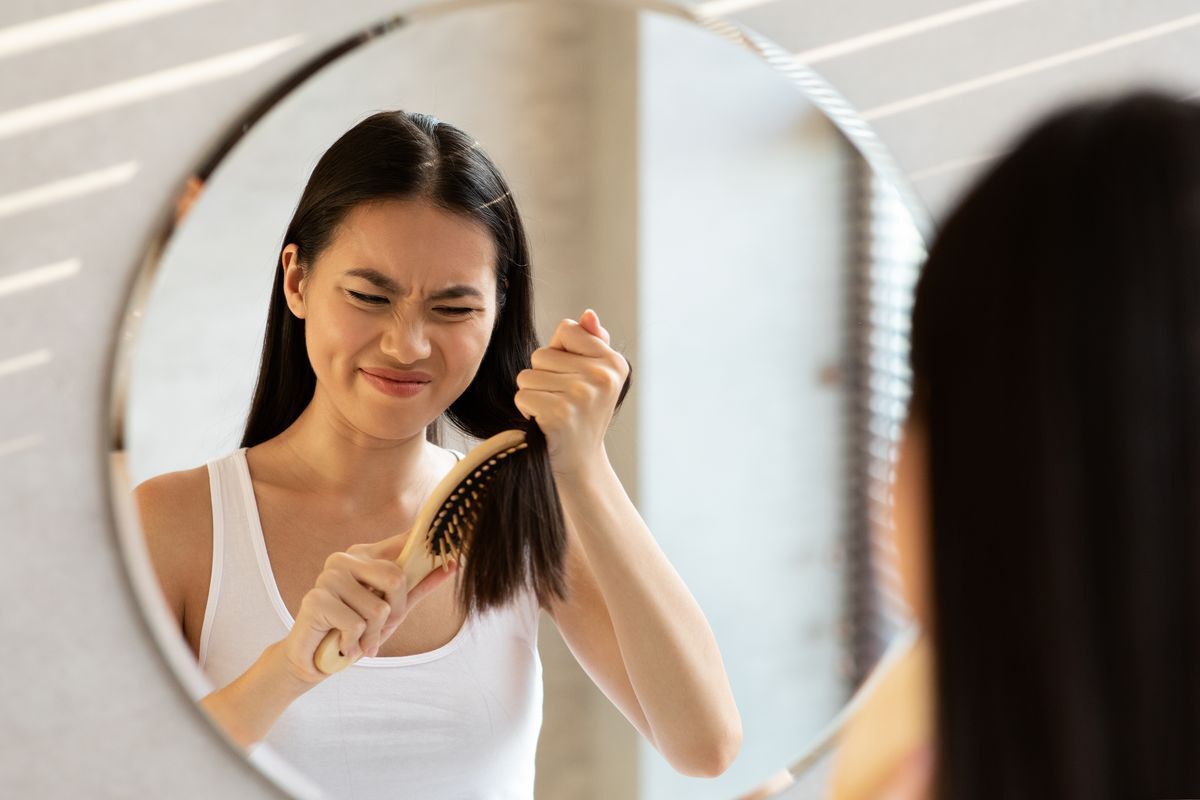 Filipino woman frustrated, trying to brush frizzy hair in the mirror