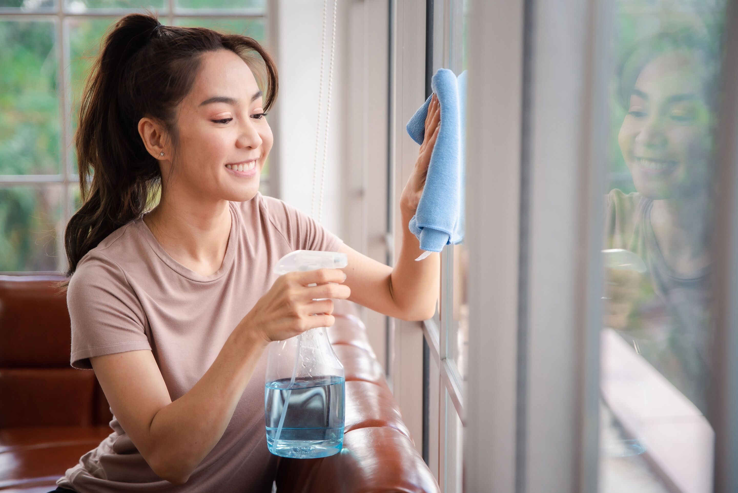 An Asian woman wearing a ponytail and t shirt, wiping and spraying windows