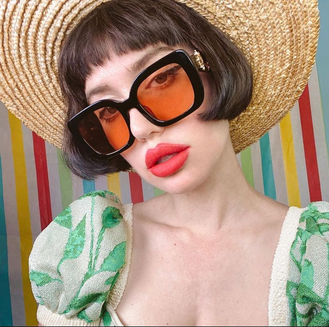 Woman with French bob and microbangs wearing a dress and tinted sunglasses. 
