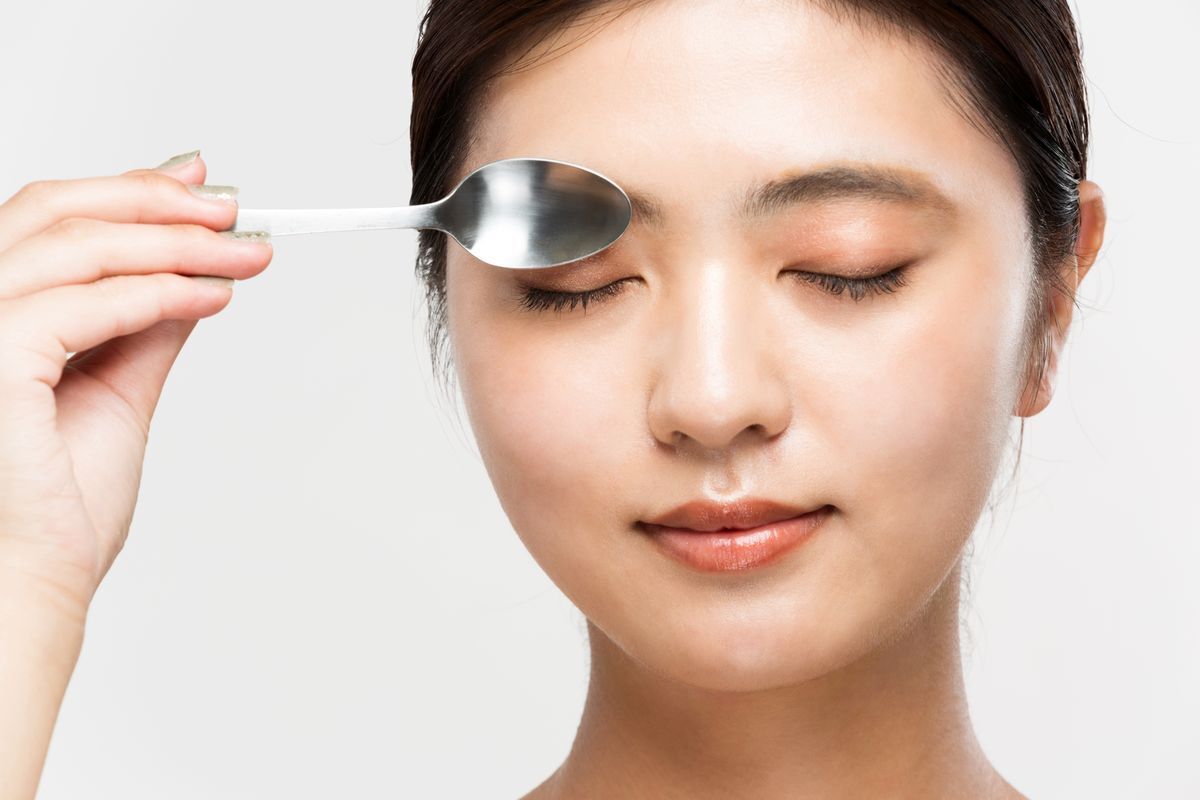A woman placing a spoon on top of her closed eye.