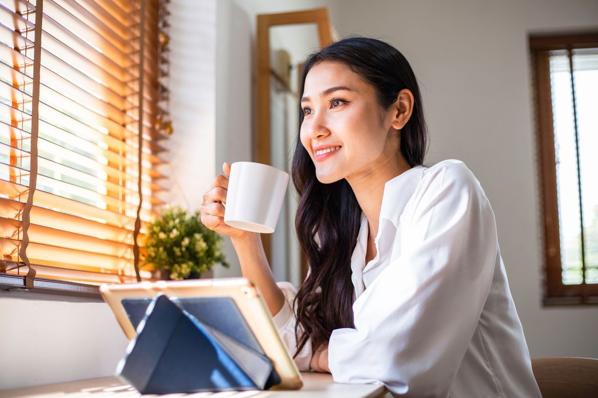 A woman staring outside a window while holding a cup of coffee.