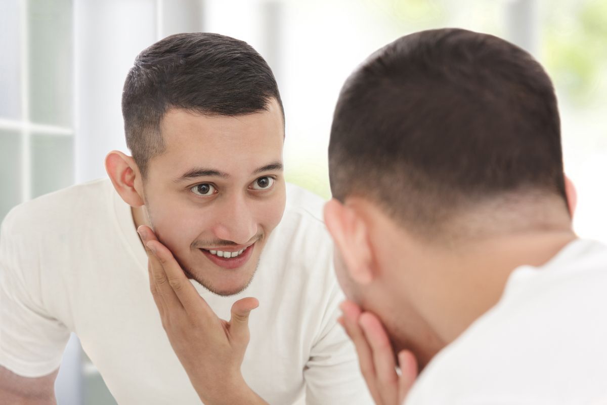 Asian man is looking at his face in the mirror, smiling.