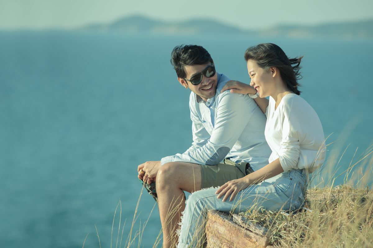 Asian couple happily sitting on a seaside cliff