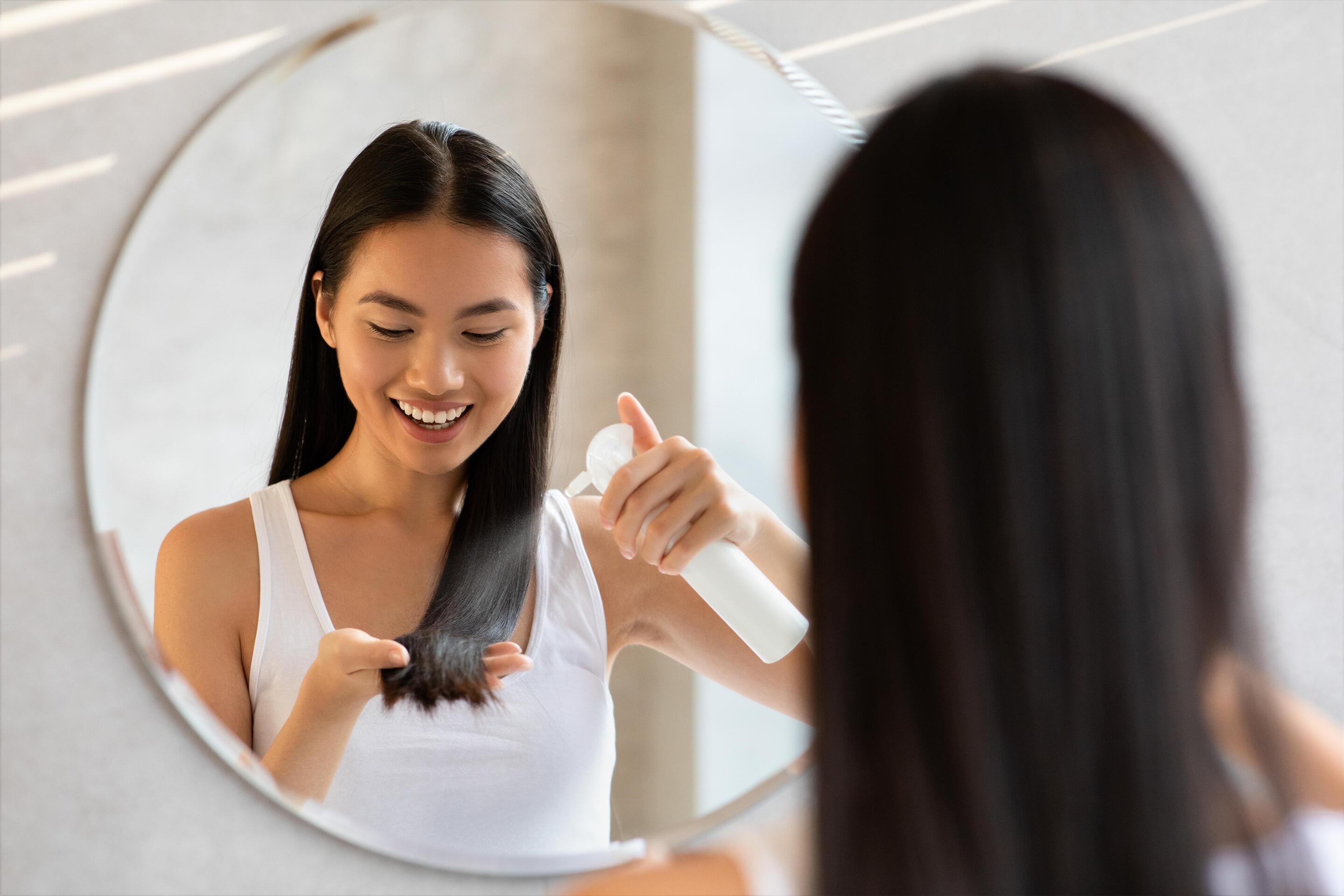 Asian woman spraying hair in front of mirror 