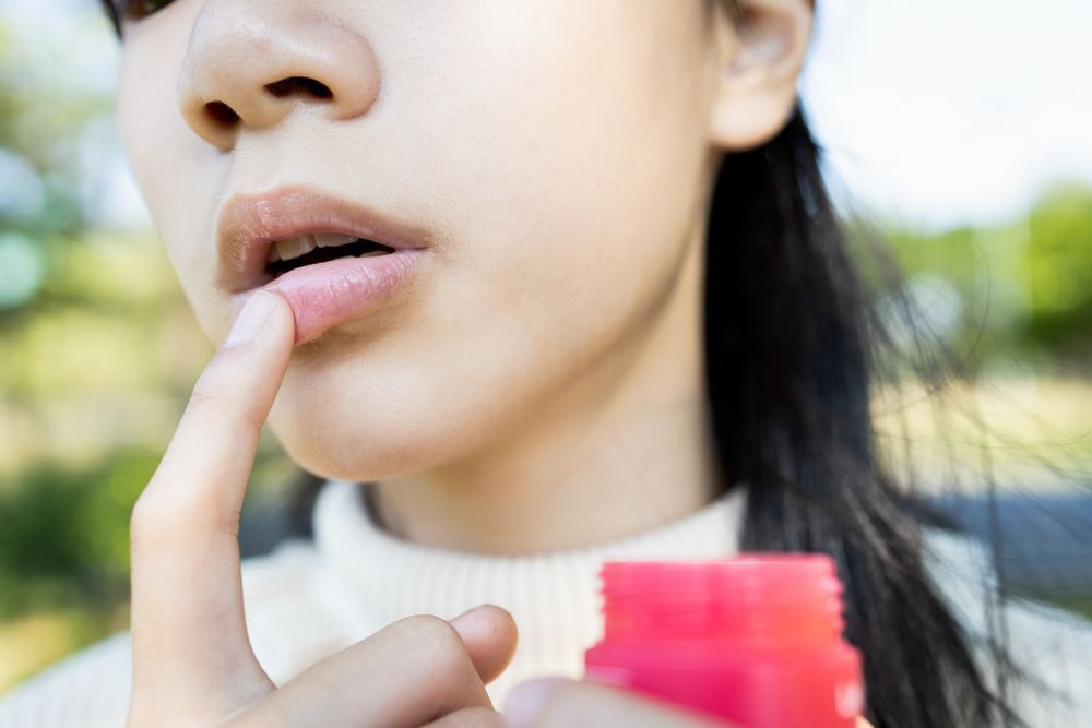 Asian girl applying lip balm from a pink pot.