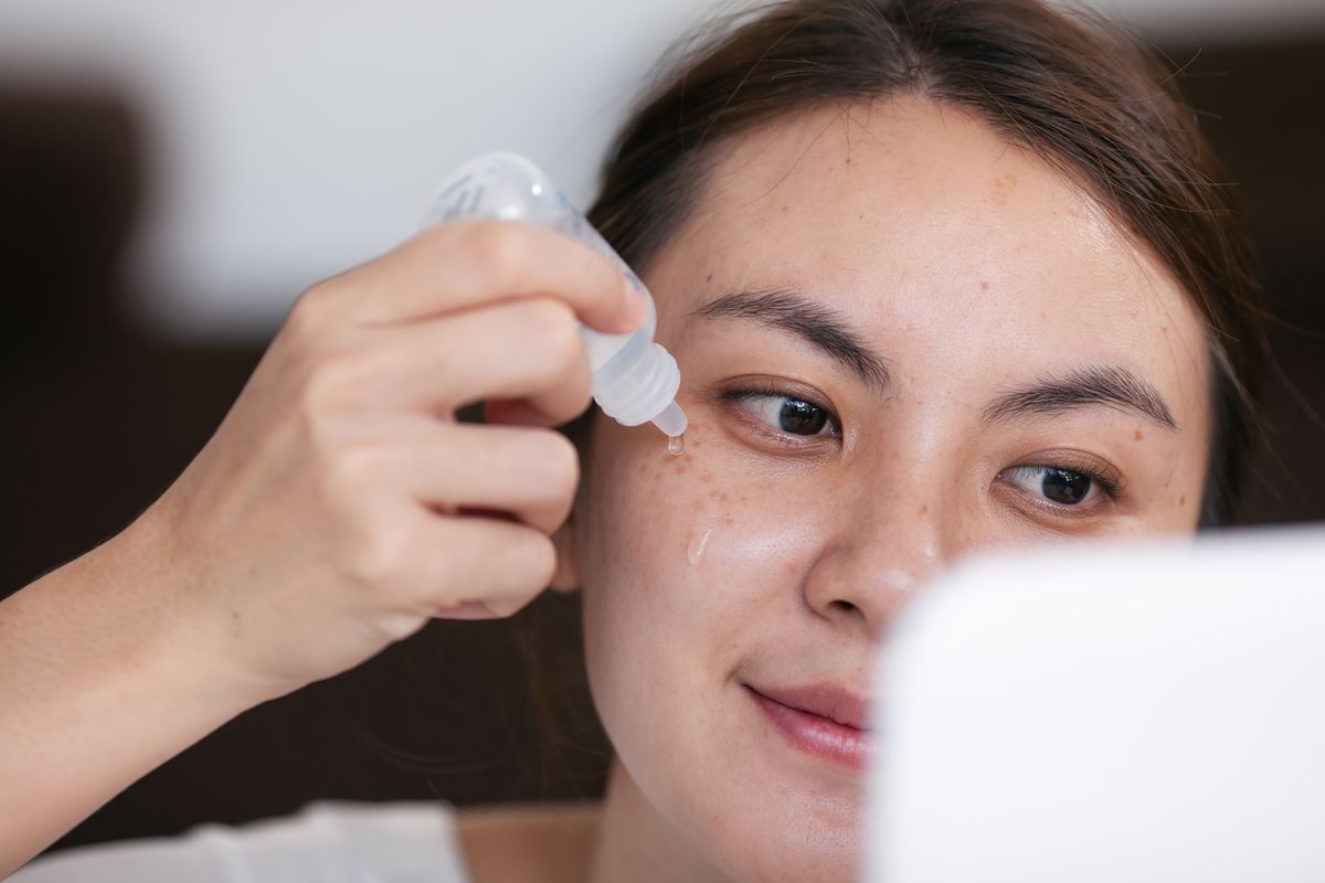 Filipino woman applying serum on her face while looking at mirror