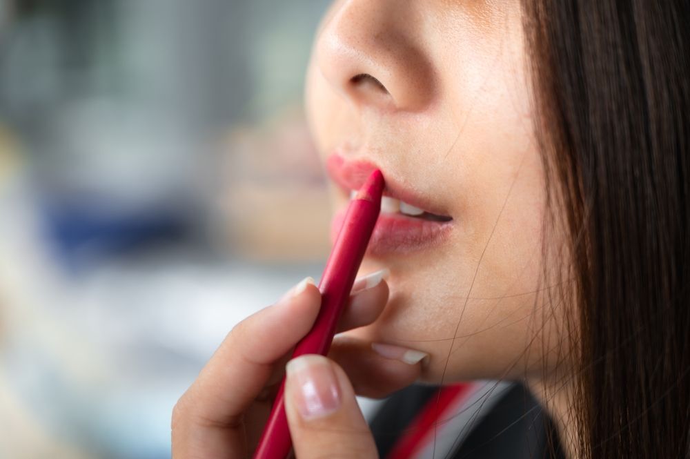 Asian woman applying pink lip liner.