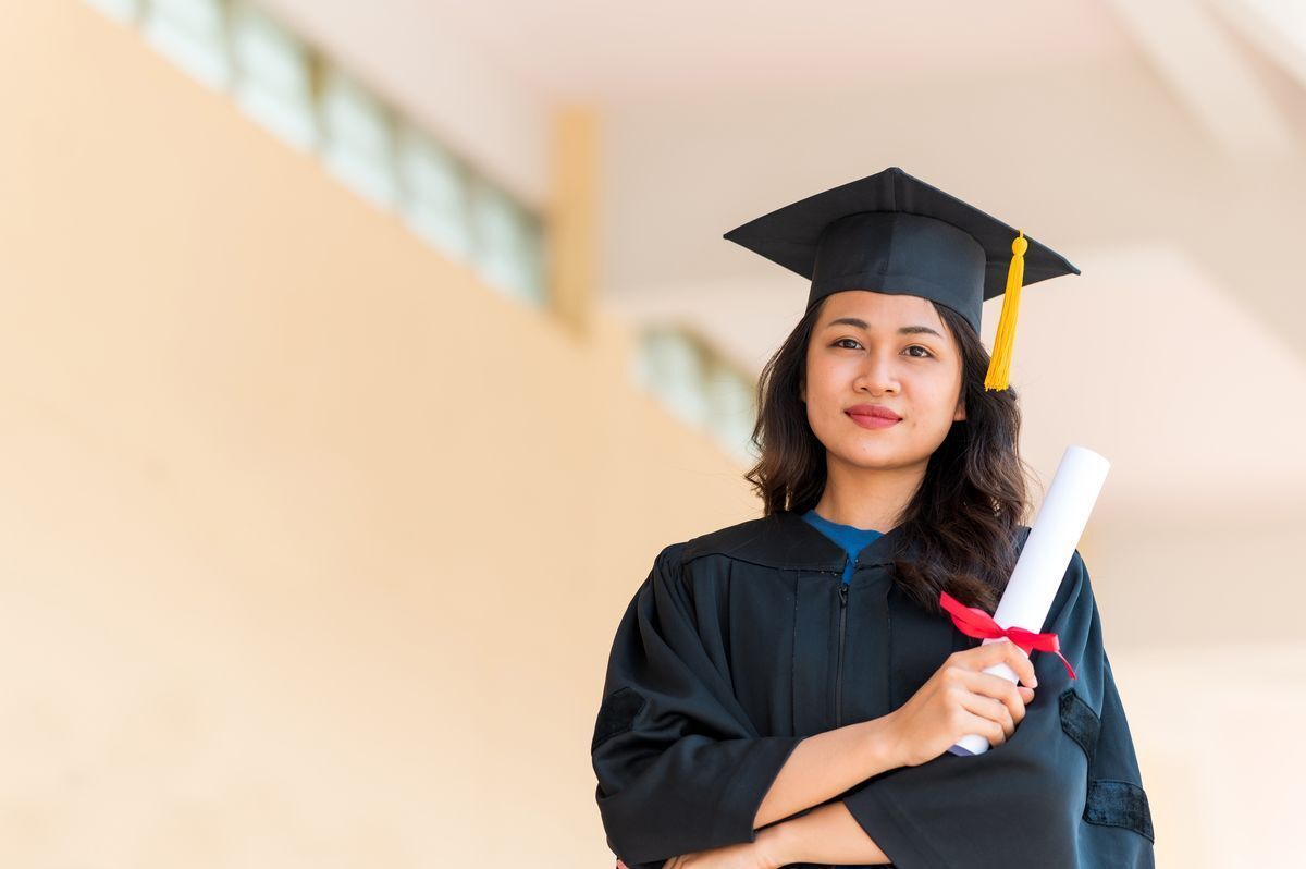 Smiling young Filipino woman holding a diploma at graduation.