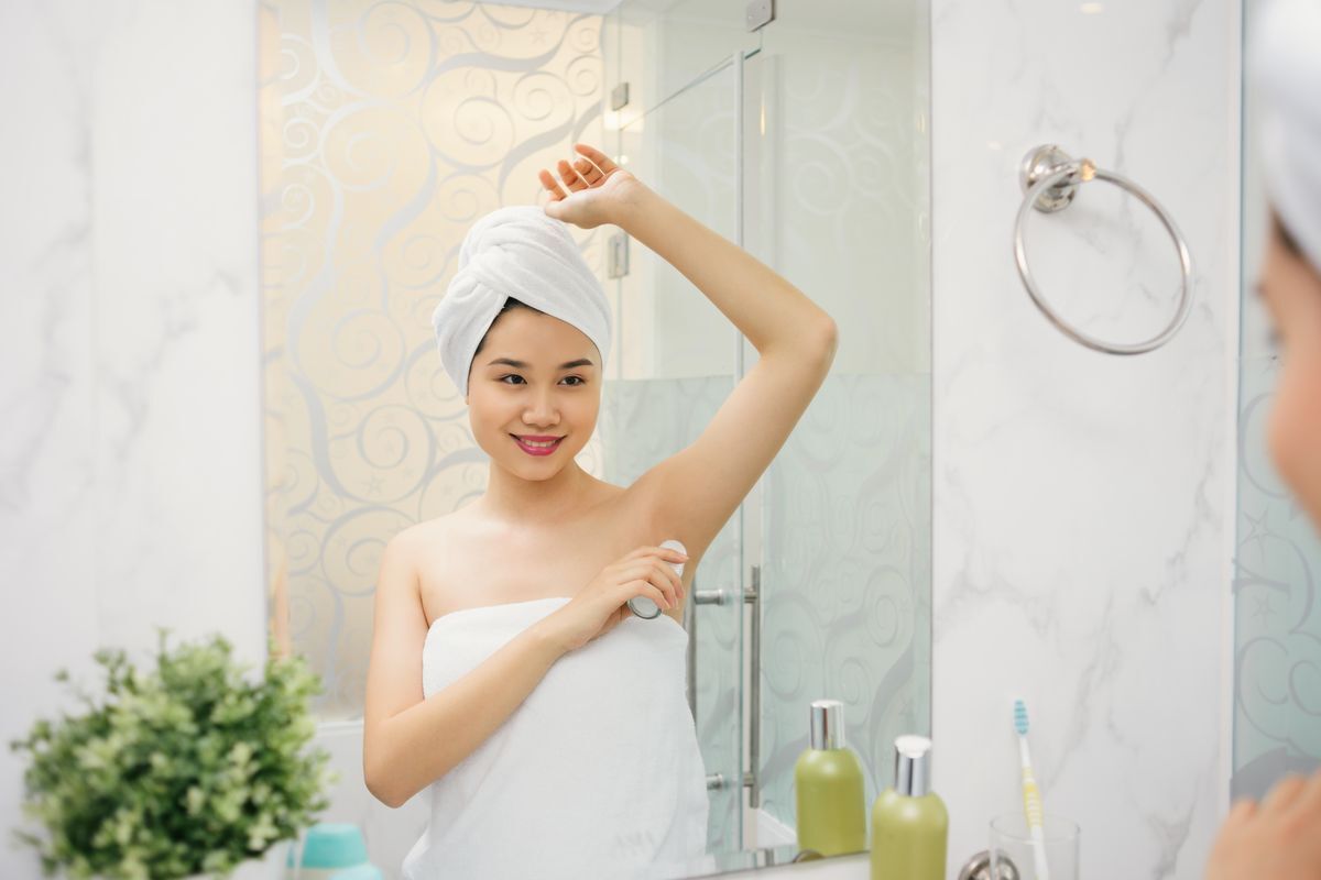 Asian woman in a towel applying roll on deodorant.