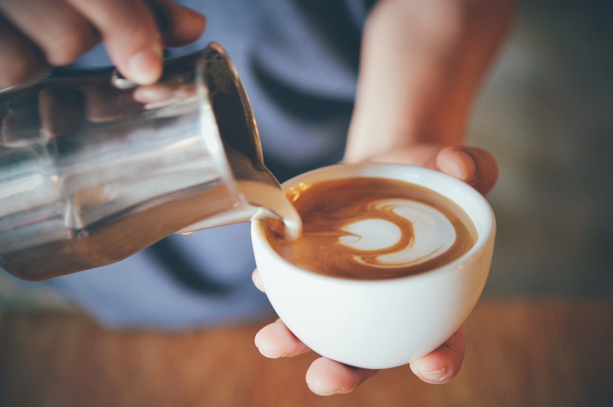 Barista pouring frothed milk into a cup of coffee making latte art. 