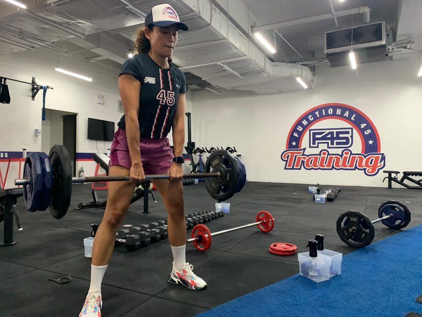Asian woman in a cap doing deadlifts at the gym.