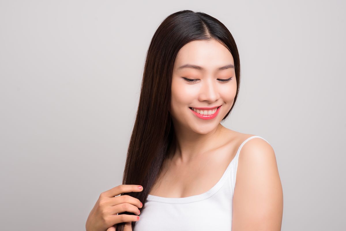 Smiling Asian female touching her hair against a grey background.