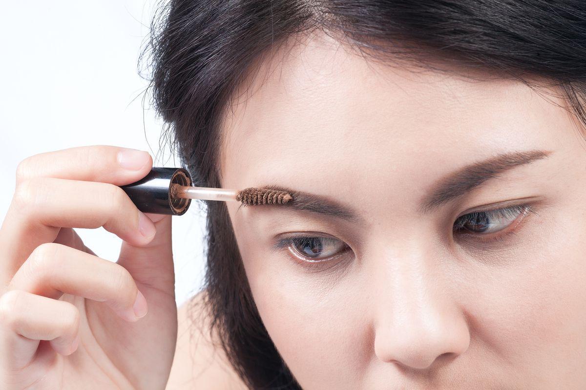 Asian woman applying brow mascara 
