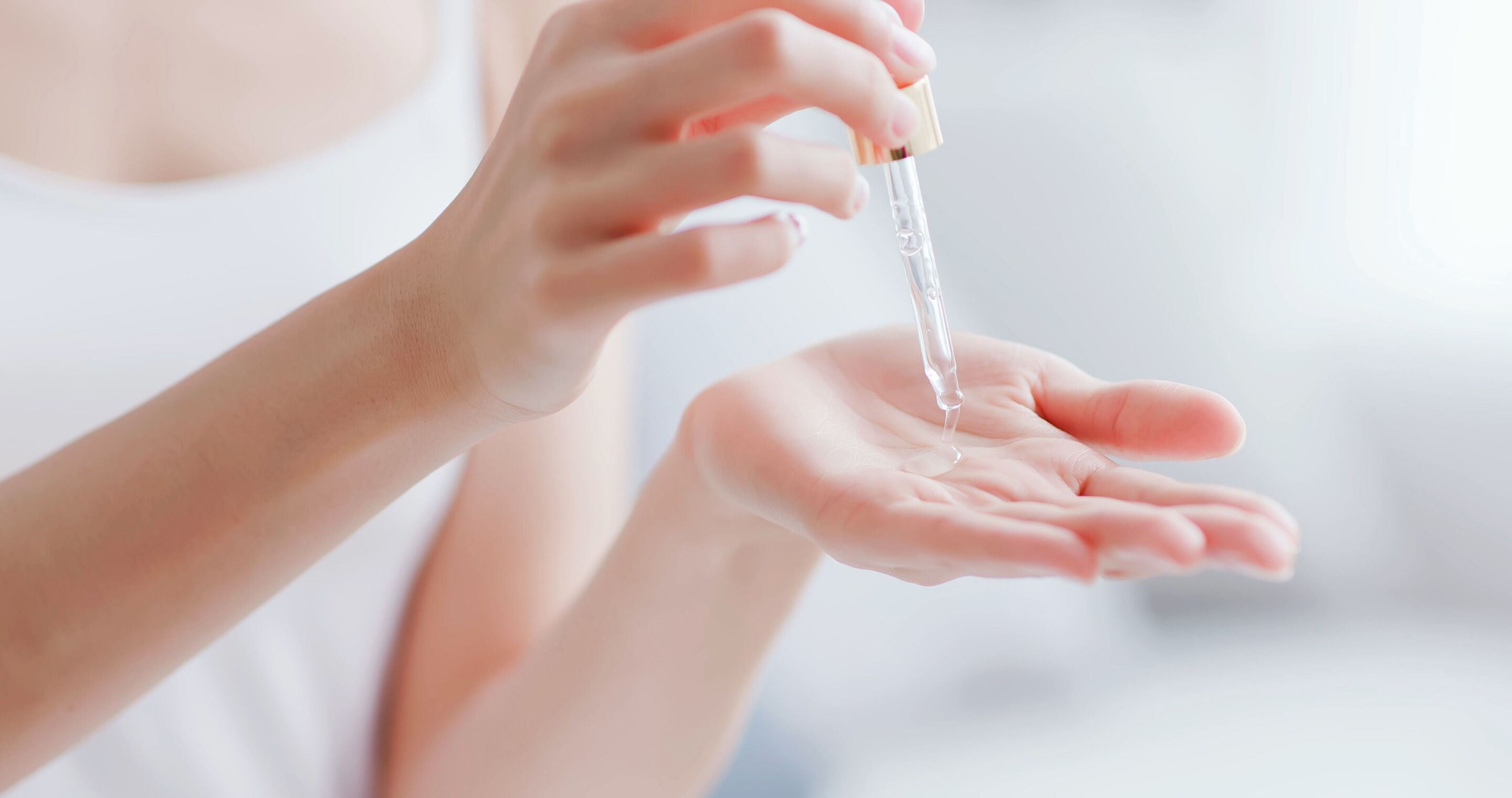Hands of a woman holding a dropper dispensing serum