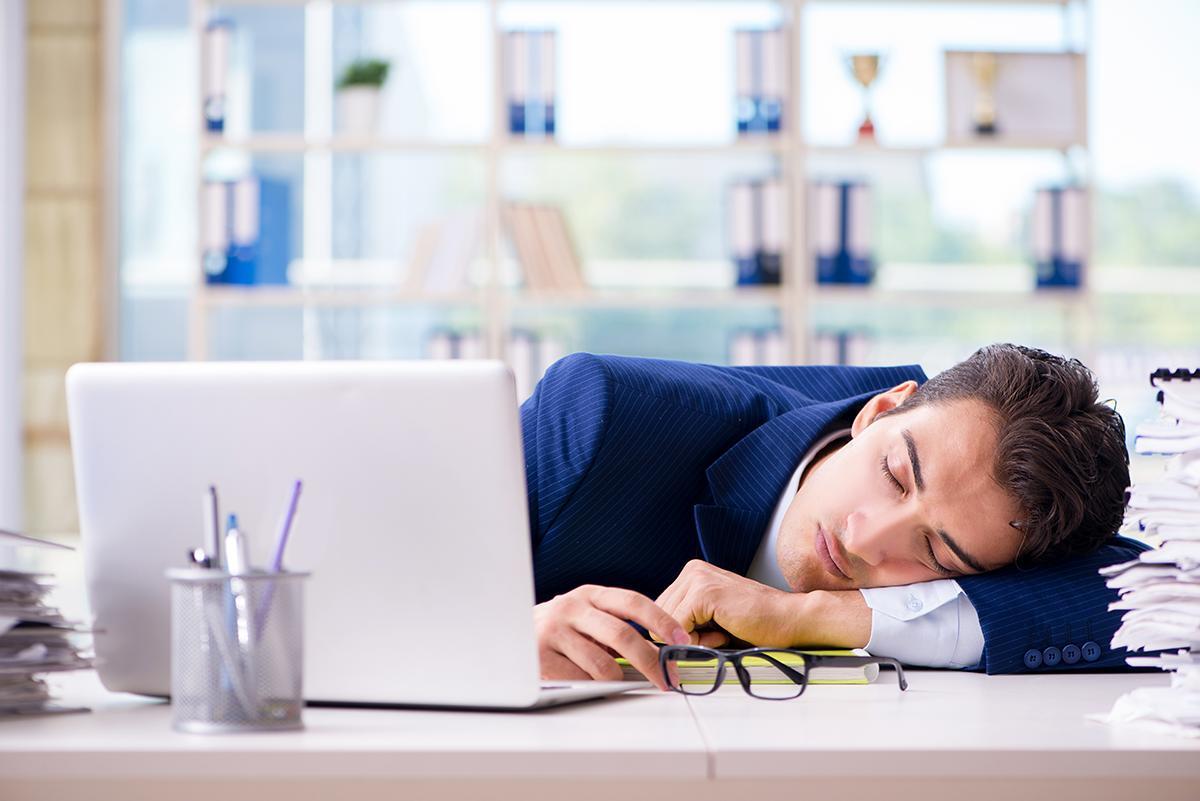 A man takes a nap on his office desk.