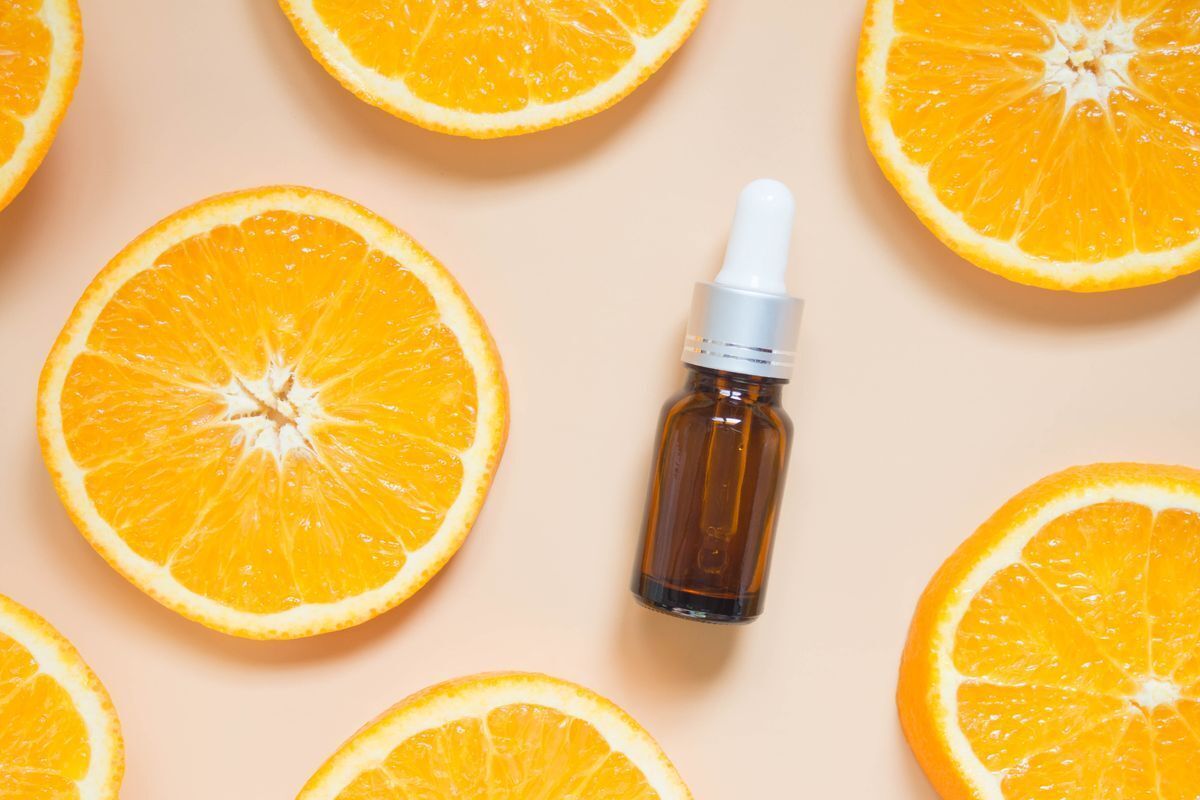 Brown bottle of serum with orange slices against a pink background. 