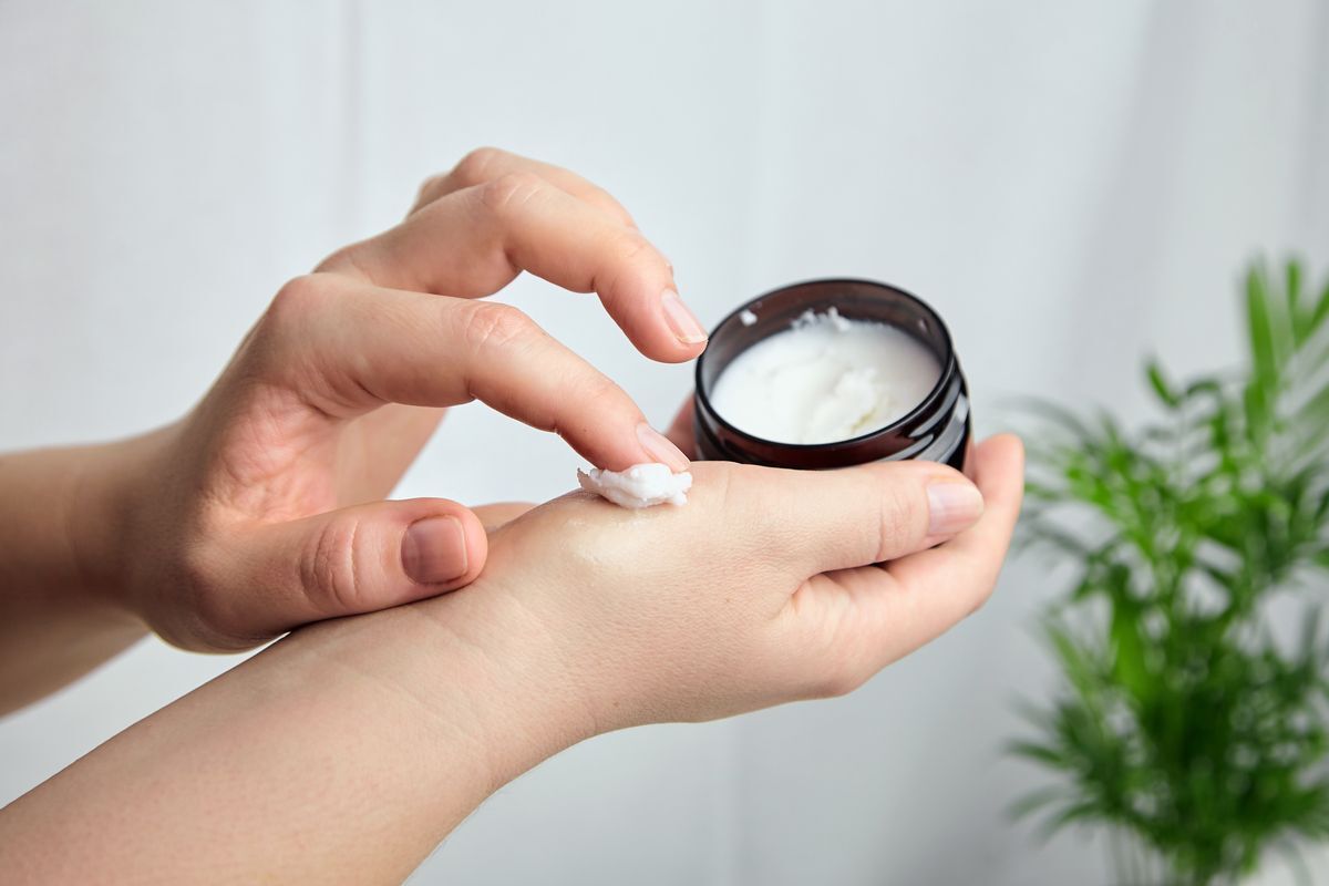 A pair of hands holding a jar of moisturizer and applying.