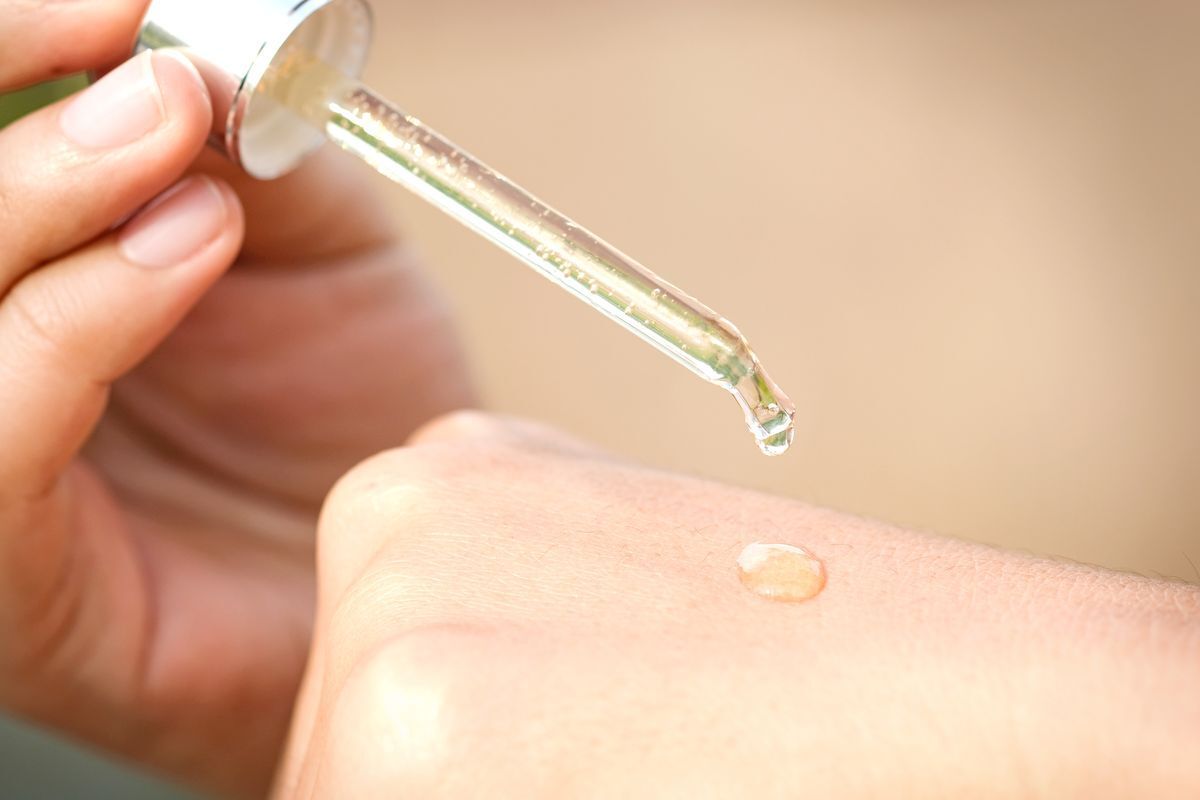 A hand holding a serum dropper and dispensing product.