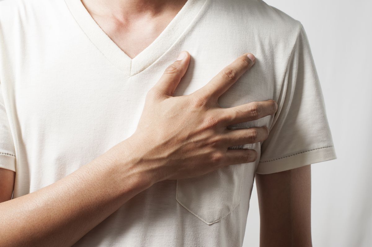 A man in a white t shirt holds his left hand to his chest.
