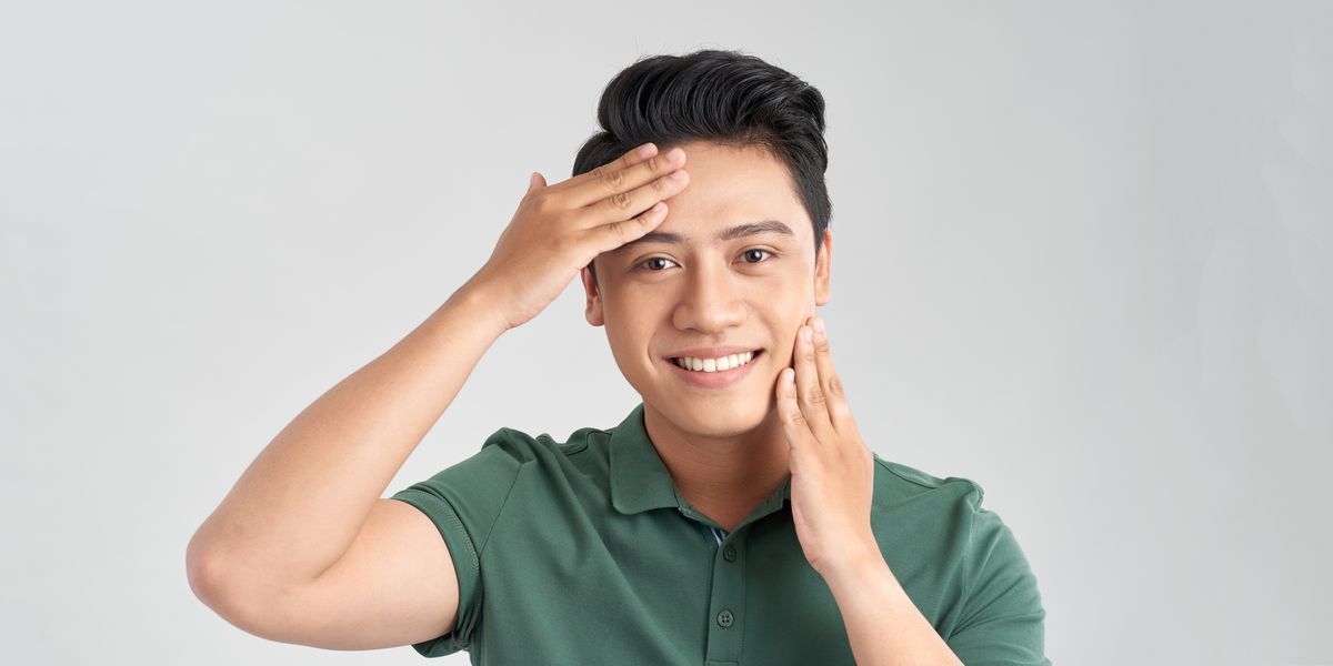 A smiling man touches his forehead and neck.