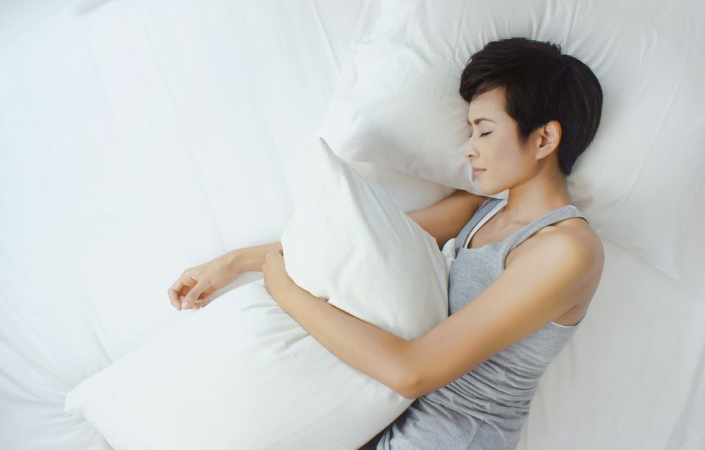 An Asian woman sleeping while holding a pillow.