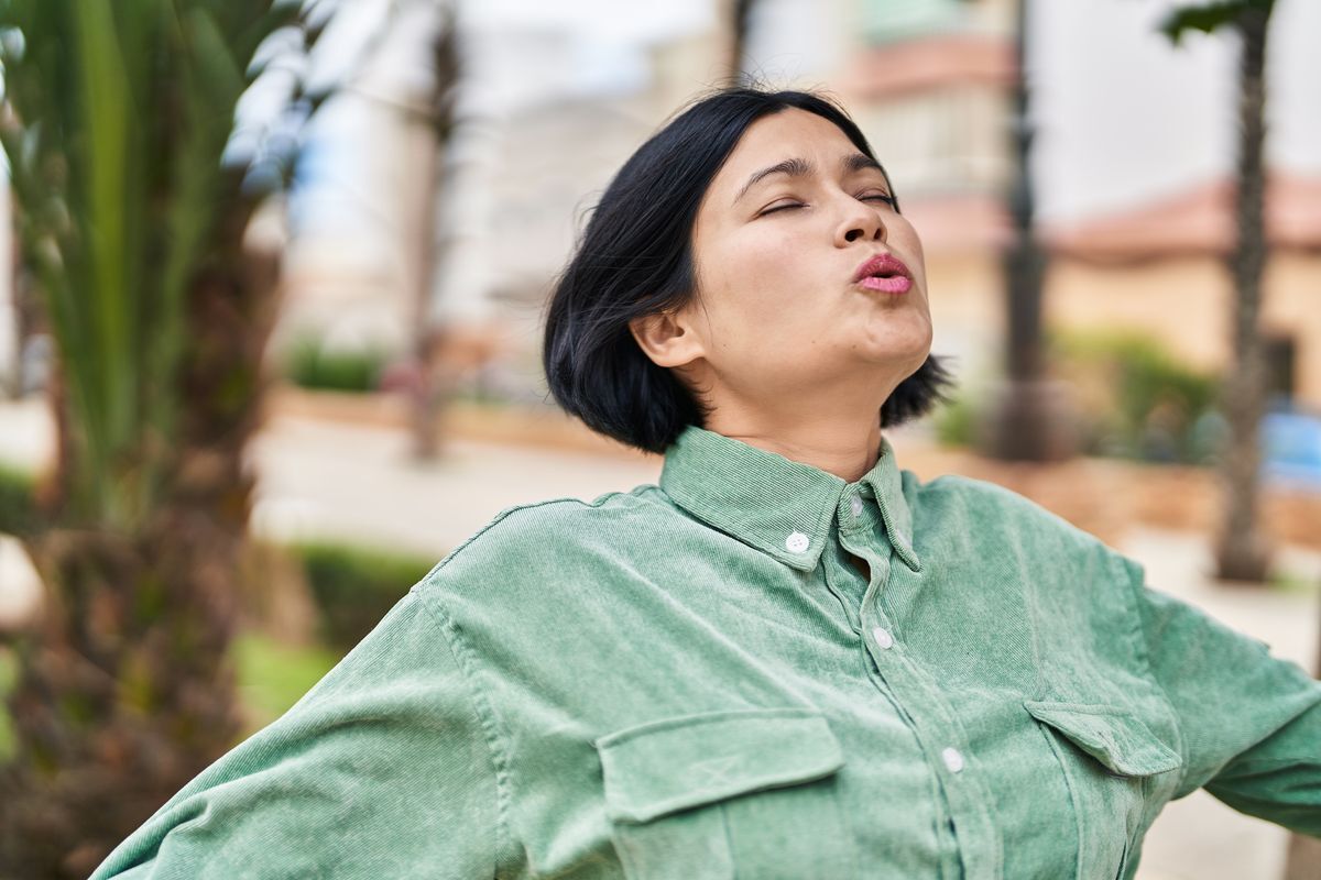 Woman taking a deep breath while walking in a park.
