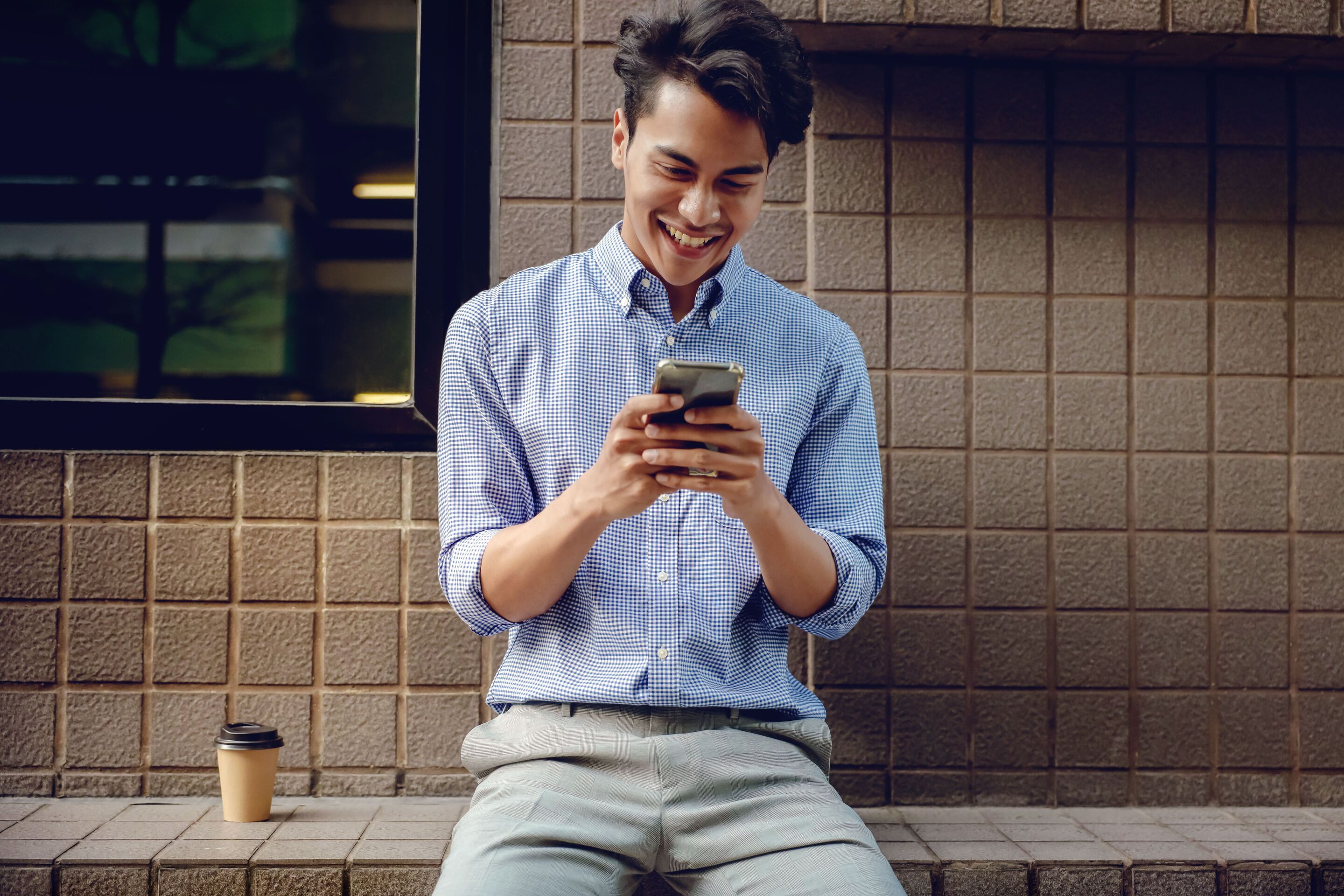 Young Asian man looking at phone while smiling and sitting down