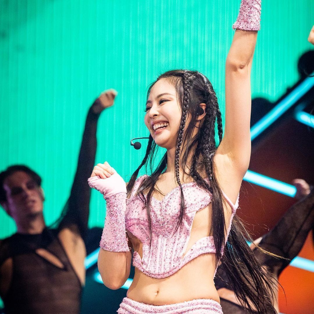 BLACKPINK’s Jennie smiling and lifting one arm up in the air during a Coachella performance.