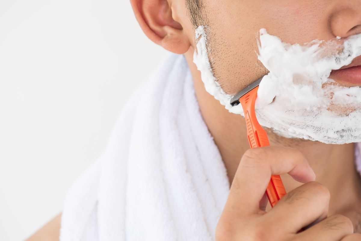 Cropped image showing a man shaving his face with foam and a towel on his neck 
