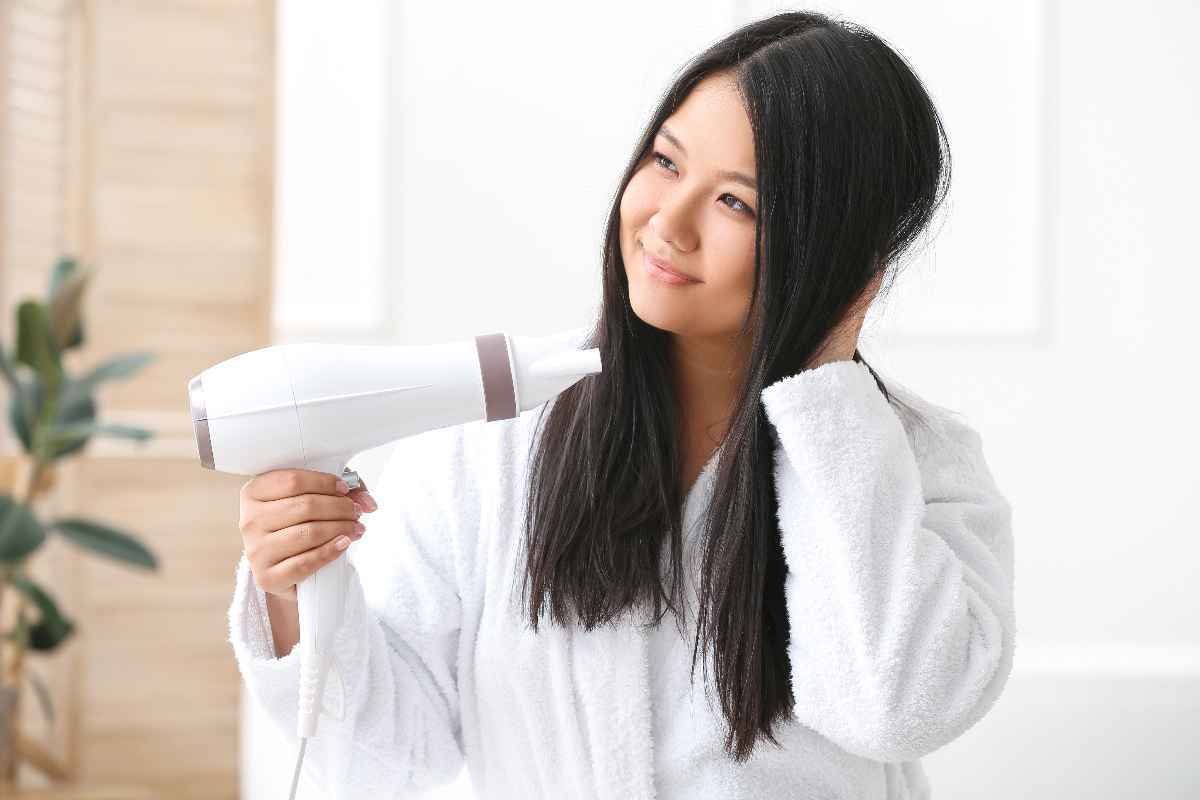 Woman drying her long hair with a white hairdryer.