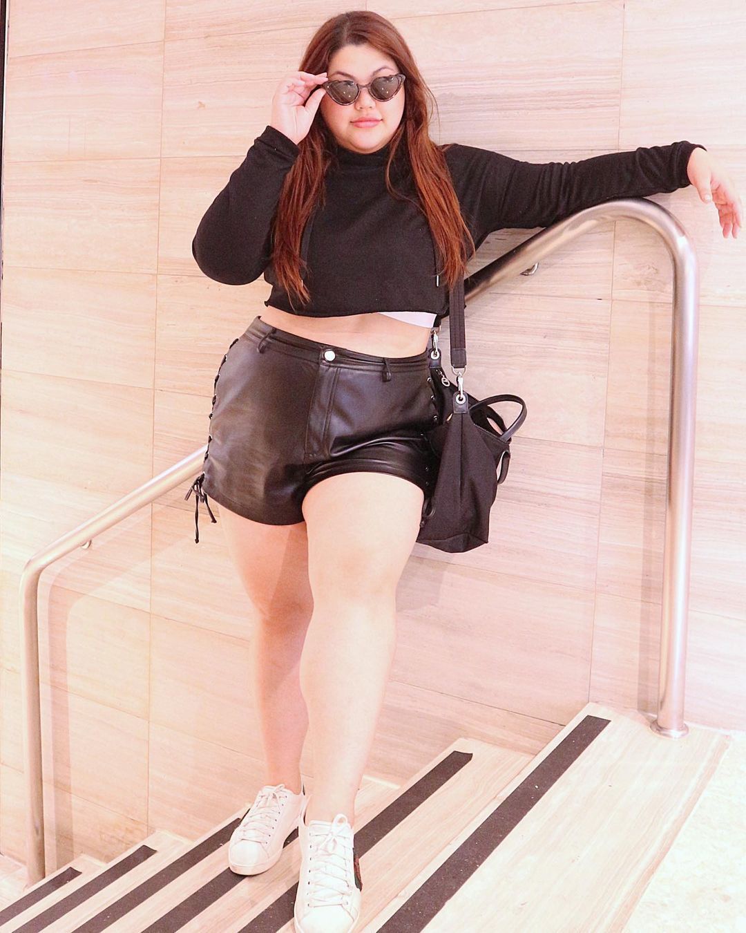 A portrait of woman wearing leather shorts and long-sleeve crop top.